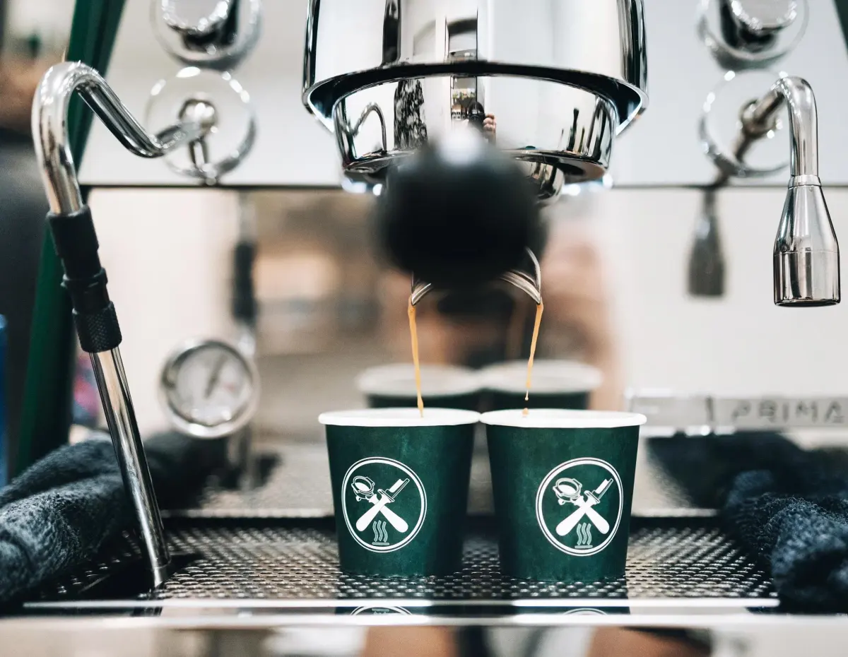 Zwei grüne gebrandete Kaffeebecher unter der Siebträgermaschine