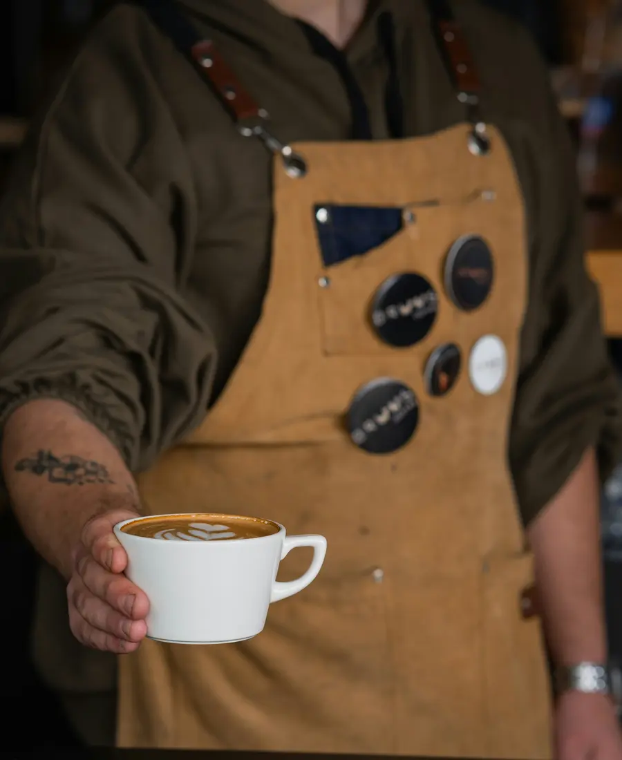 Barista mit Schürze reicht einen Cappuccino